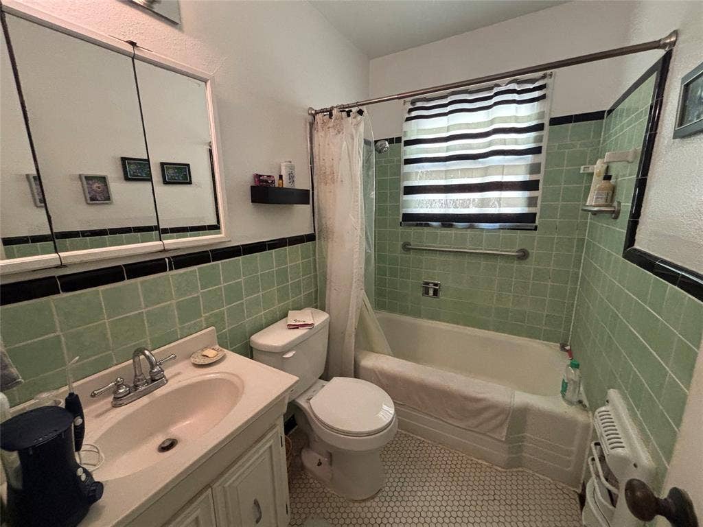Bathroom featuring light green wall tiles with black trim, a white vanity with an integrated sink, a built-in bathtub with a shower, and honeycomb-patterned floor tiles