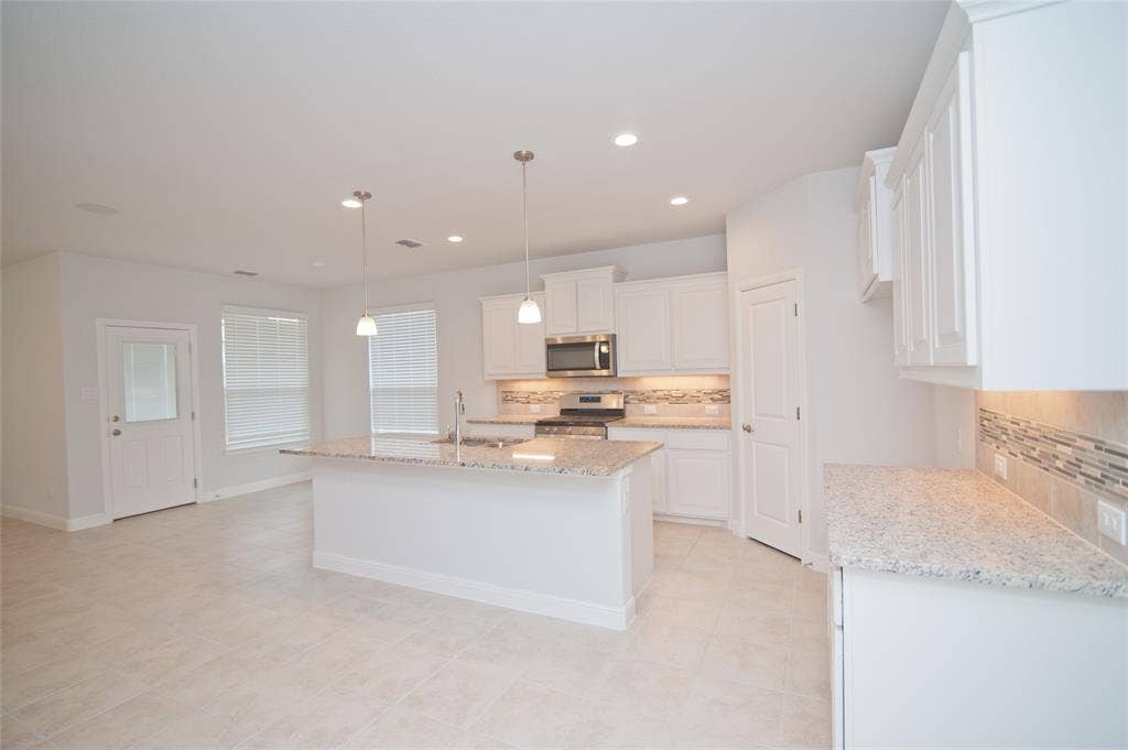 1021 Gillespie Drive, Fort Worth, TX 76247 Open-concept kitchen featuring an eat-at island, granite countertops, white cabinetry, and stainless steel appliances