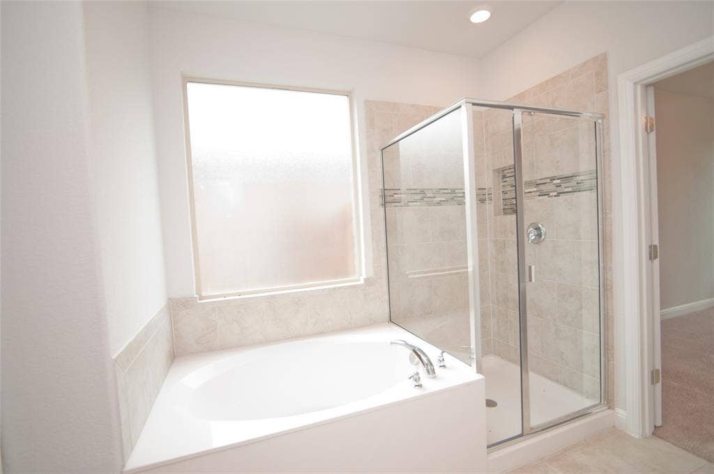 1021 Gillespie Drive, Fort Worth, TX 76247 Alcove soaking tub with chrome fixtures, glass-enclosed shower with tiled walls and decorative accent band, and recessed lighting