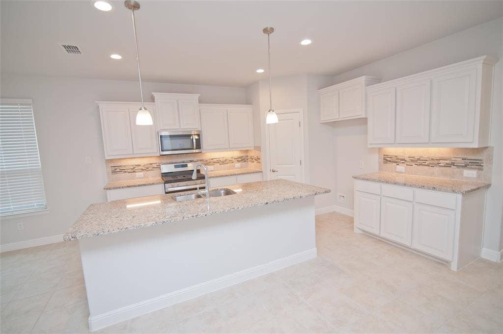 1021 Gillespie Drive, Fort Worth, TX 76247 Kitchen featuring a central island with a double basin sink, stainless steel appliances, white cabinetry, granite countertops, and a tile backsplash