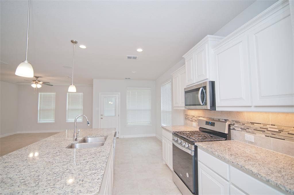 1021 Gillespie Drive, Fort Worth, TX 76247 Kitchen featuring white cabinetry, light-toned countertops, stainless steel appliances, and a mosaic tile backsplash