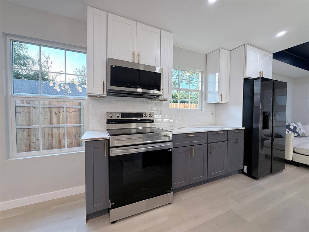 2538 Hooper Street, Dallas, TX 75215 Kitchen featuring two-tone cabinetry, stainless steel appliances, white subway tile backsplash, light wood-finish flooring, and white countertops