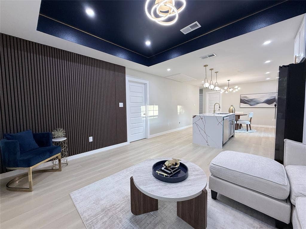 2538 Hooper Street, Dallas, TX 75215 Dark wood-slat accent wall, recessed ceiling with perimeter lighting, light wood-finish flooring, kitchen island with waterfall counter, and modern pendant lighting