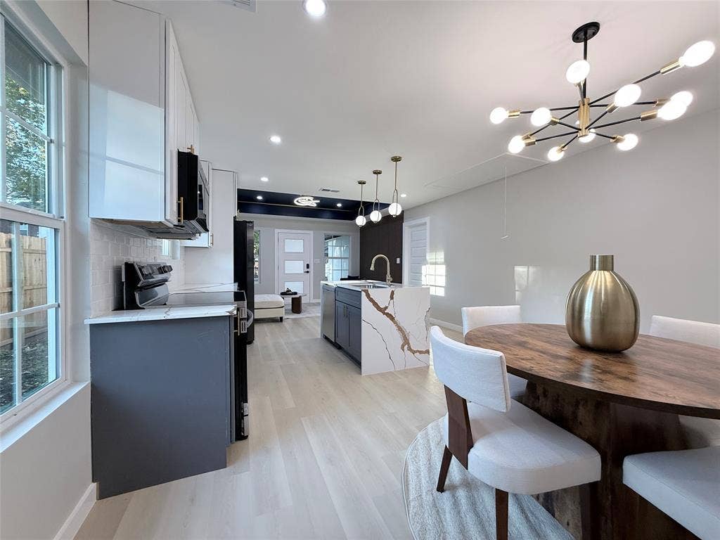 2538 Hooper Street, Dallas, TX 75215 Open-concept living area with light wood-finish flooring, a contemporary chandelier, and a kitchen island featuring a waterfall-edge countertop