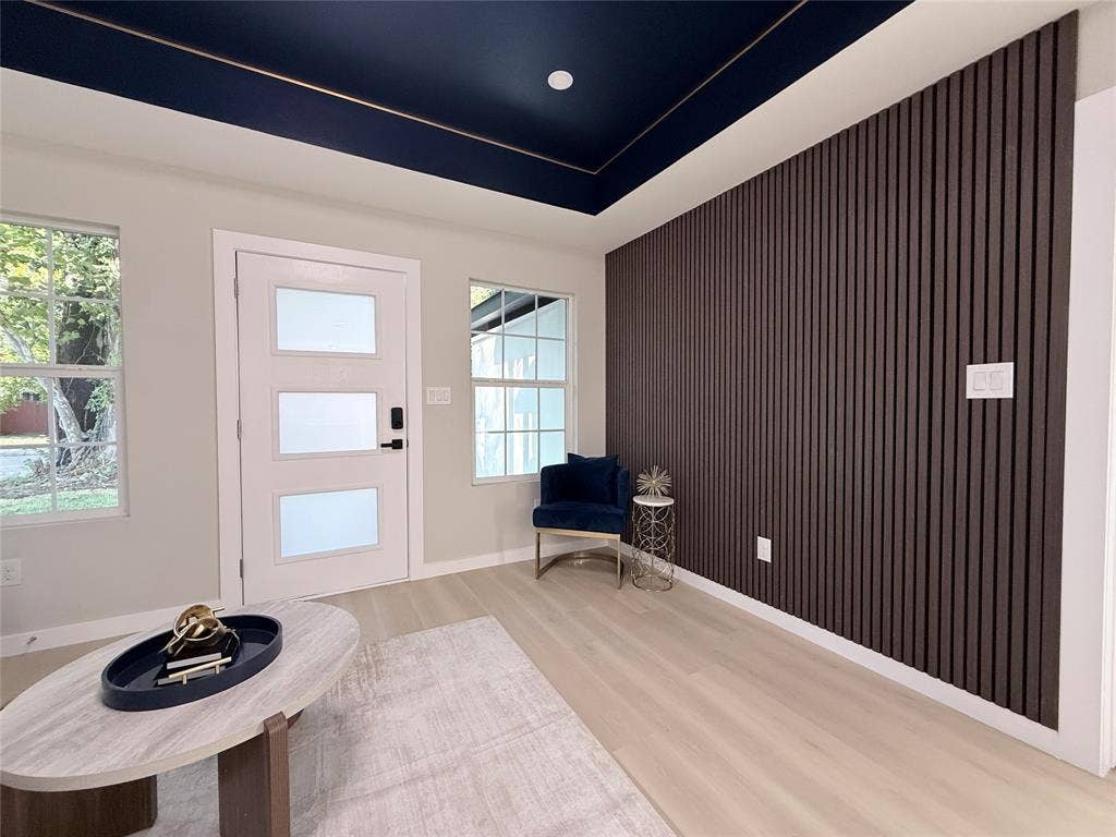2538 Hooper Street, Dallas, TX 75215 Dark wood panel accent wall, light wood-finish flooring, white entry door with frosted glass panels, and a dark blue ceiling with gold trim