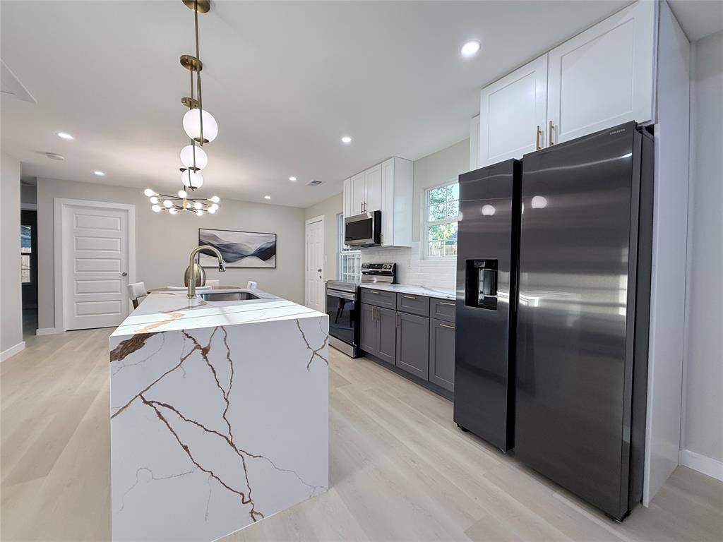 2538 Hooper Street, Dallas, TX 75215 Kitchen featuring a large waterfall island with integrated sink, stainless steel appliances, two-tone cabinetry, wood-finish flooring, and recessed lighting