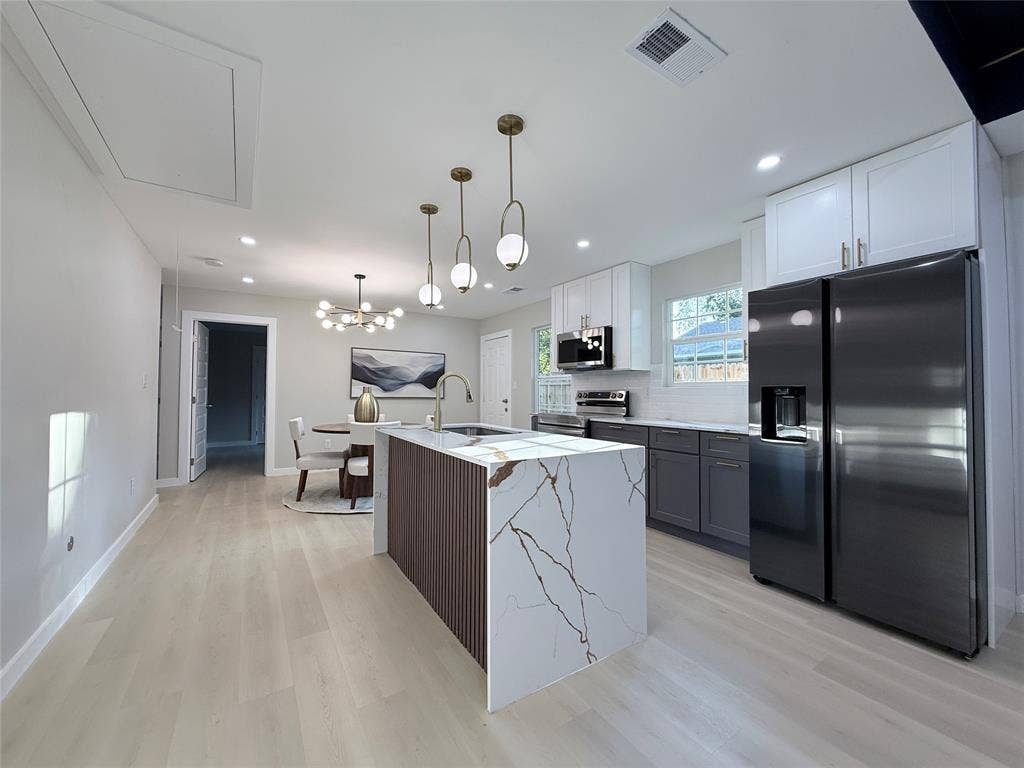 2538 Hooper Street, Dallas, TX 75215 Modern kitchen featuring an island with a waterfall countertop, contemporary pendant lighting, light wood-finish flooring, white upper cabinetry, and dark lower cabinetry