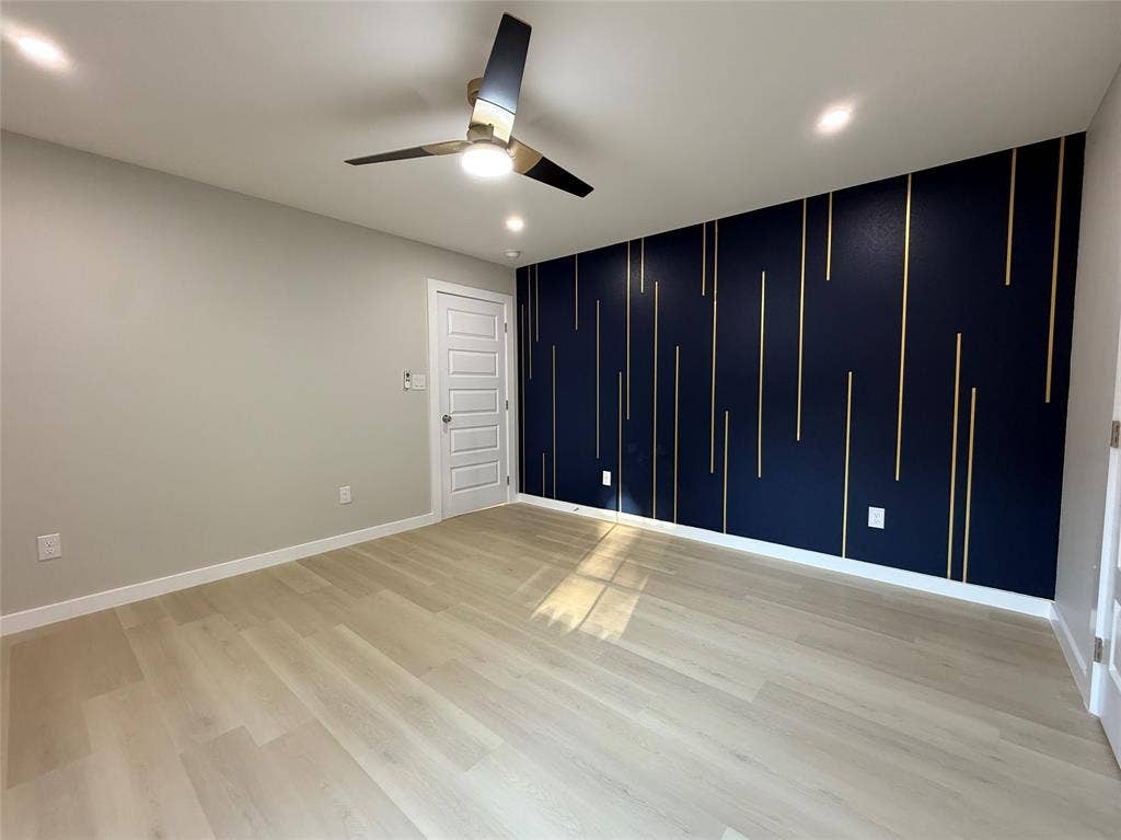 2538 Hooper Street, Dallas, TX 75215 Modern ceiling fan with integrated lighting, recessed ceiling lights, light wood-finish flooring, a paneled interior door, and a navy accent wall with vertical gold detailing