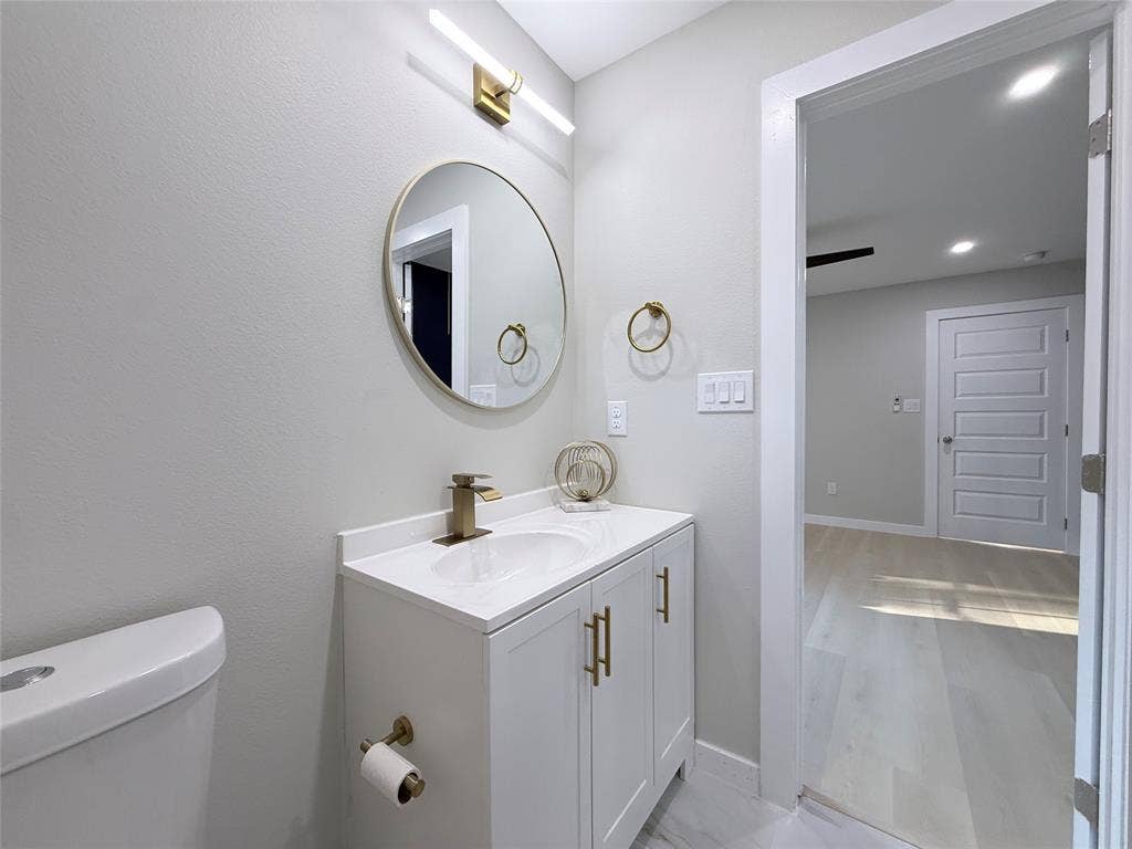 2538 Hooper Street, Dallas, TX 75215 White vanity with gold-finish hardware, a circular mirror, and a gold-finish faucet