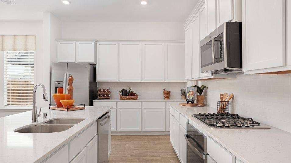 Kitchen featuring white cabinetry, light-toned countertops, stainless steel appliances, a double basin sink, and a built-in microwave
