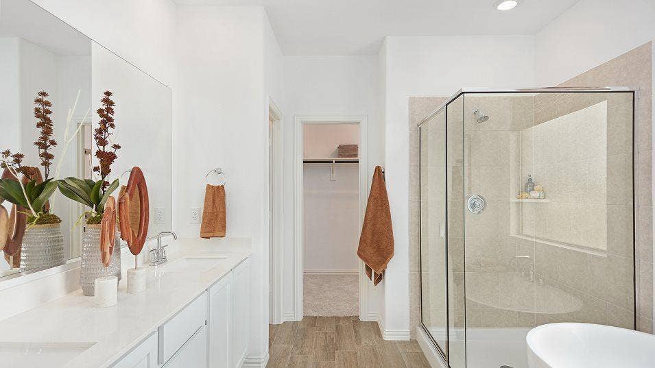 Double vanity with integrated sinks, wood-finish flooring, recessed lighting, walk-in shower with glass enclosure, and built-in shelving