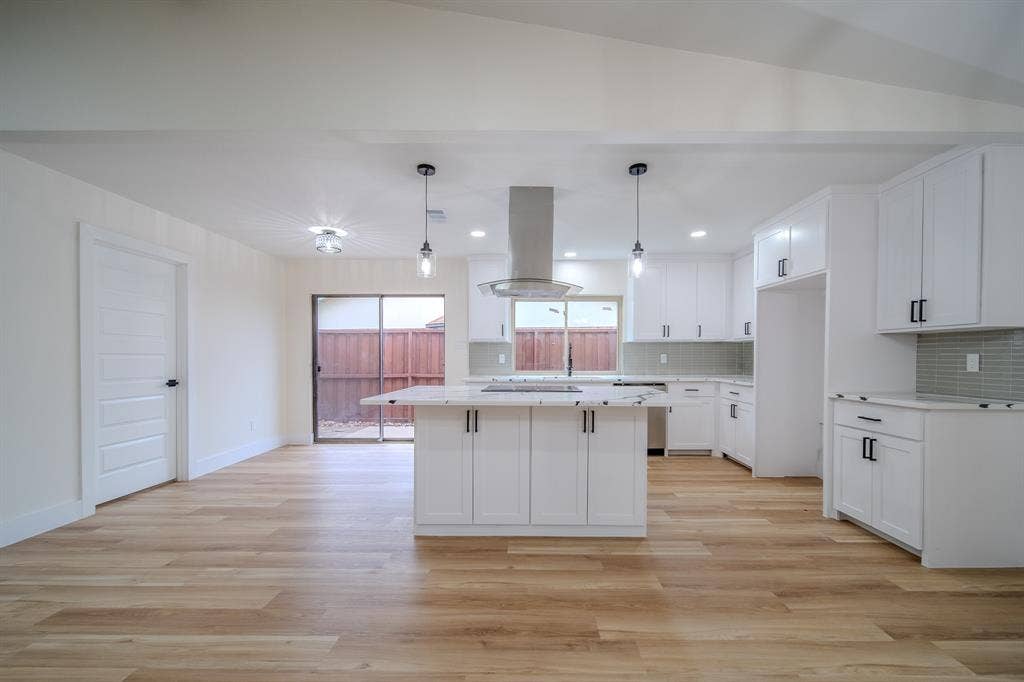 Vaulted ceilings with recessed lighting, wood-finish flooring, white shaker cabinetry with black hardware, a kitchen island with a cooktop, and a tile backsplash