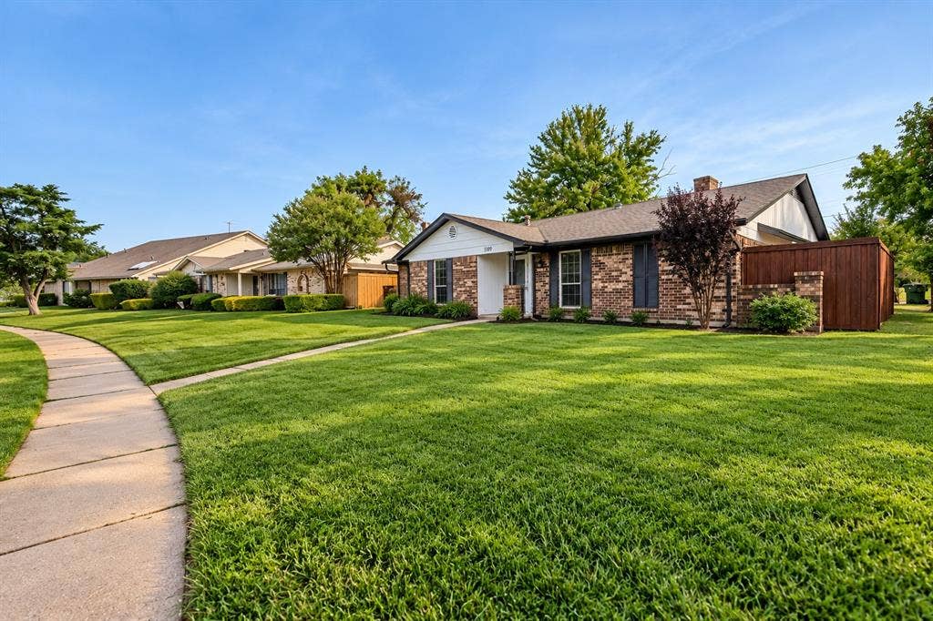 Brick facade home with a shingle roof, mature landscaping, and an adjacent privacy fence