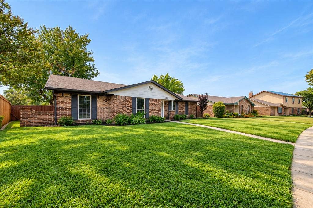 Brick exterior with dark shutters, front landscaping, and a well-maintained lawn