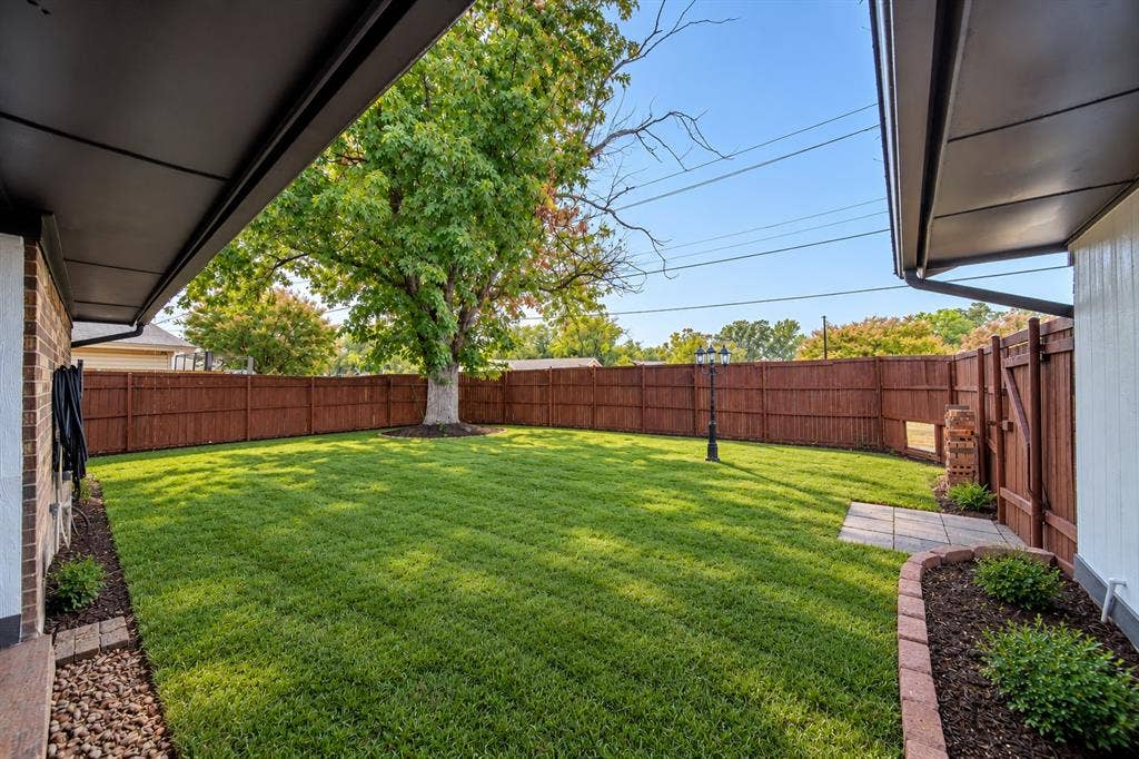 Expansive backyard featuring a lush lawn, privacy fencing, mature trees, and a paved patio area(staged with grass)