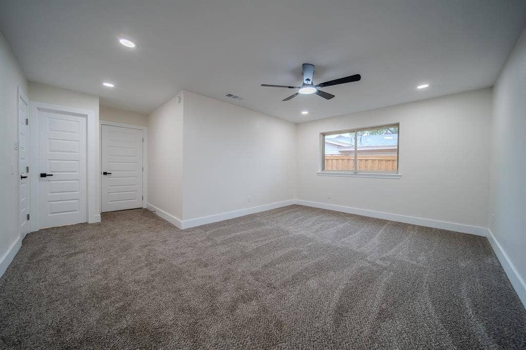 Spacious room with plush gray carpeting, recessed lighting, white panel doors with black hardware, a ceiling fan, and an exterior window