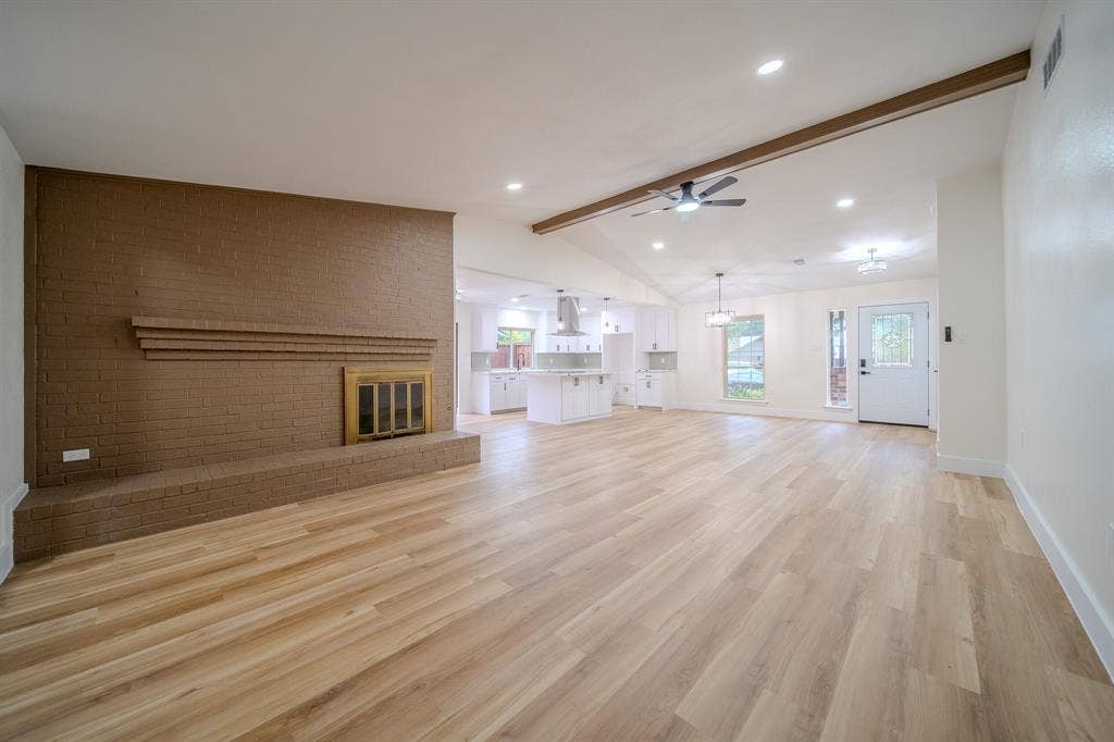 Expansive main living area featuring wood-finish flooring, a brick fireplace, and vaulted ceilings with exposed beams