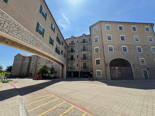 Multi-story facade featuring stucco and stone veneer, multiple balconies, a covered pedestrian bridge, arched entryway, and paver driveway
