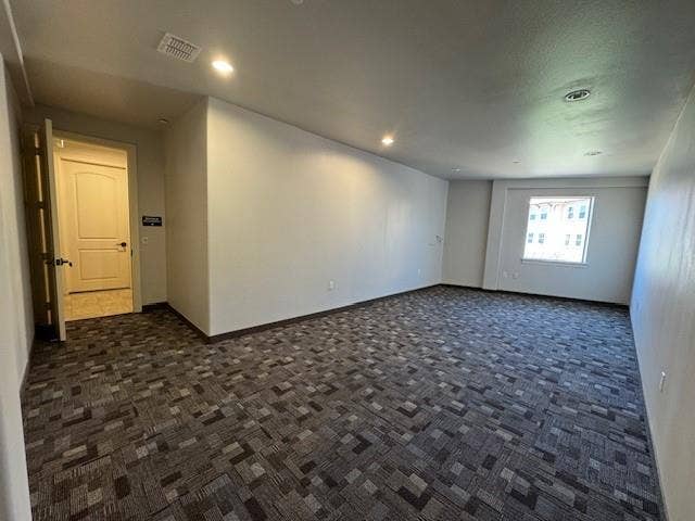 Spacious room with a patterned carpet, recessed lighting, and a white interior door with dark hardware