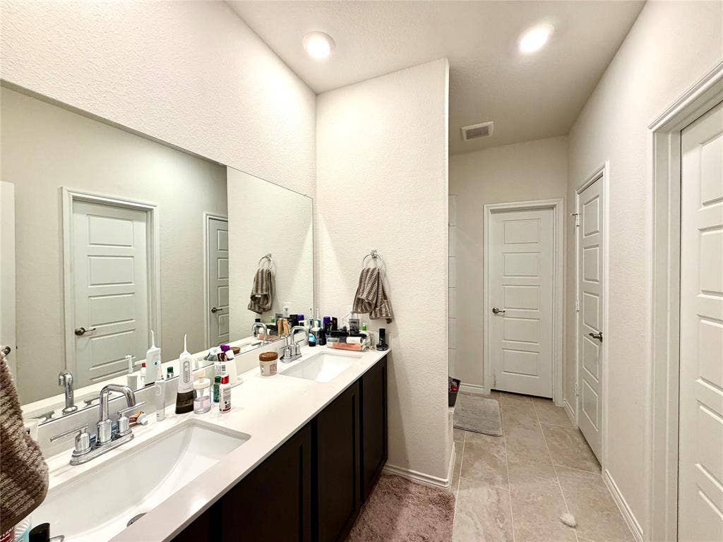 Dual vanity with integrated sinks, expansive wall-mounted mirror, recessed lighting, and tile flooring