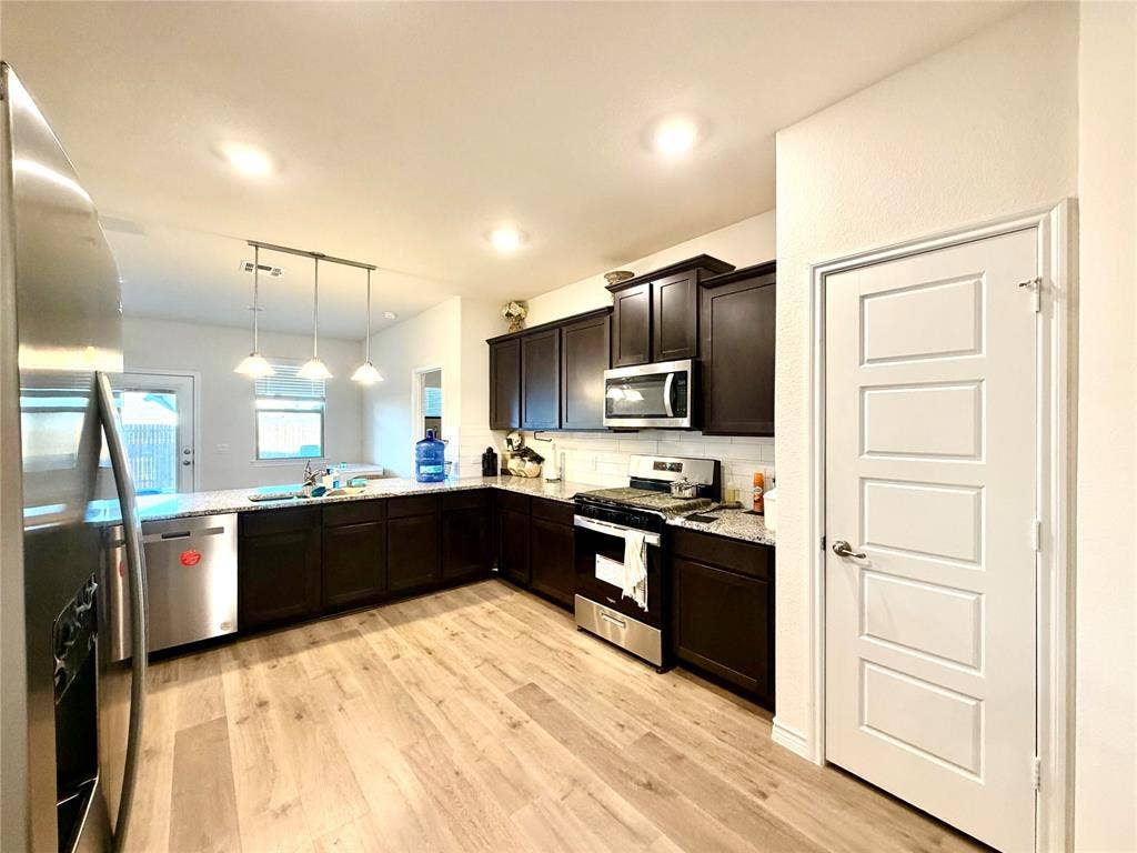 Kitchen featuring wood-finish flooring, dark wood cabinetry, stainless steel appliances, and a white subway tile backsplash