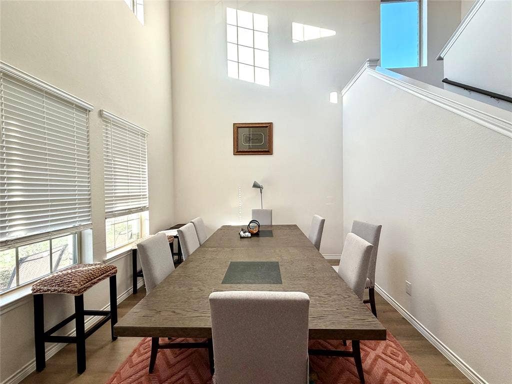 Vaulted ceiling with high transom windows and upper-level windows, wood-finish flooring, two large windows with blinds, and a staircase with a handrail