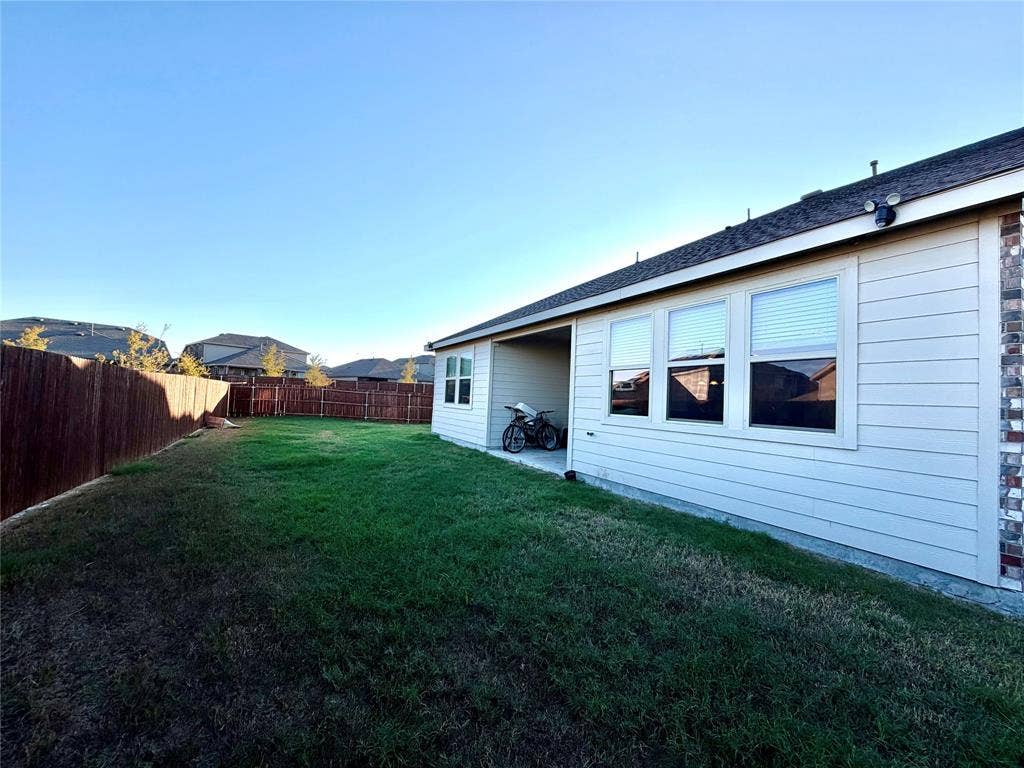 Expansive backyard featuring a manicured lawn, full privacy fencing, a covered patio, and brick exterior accents