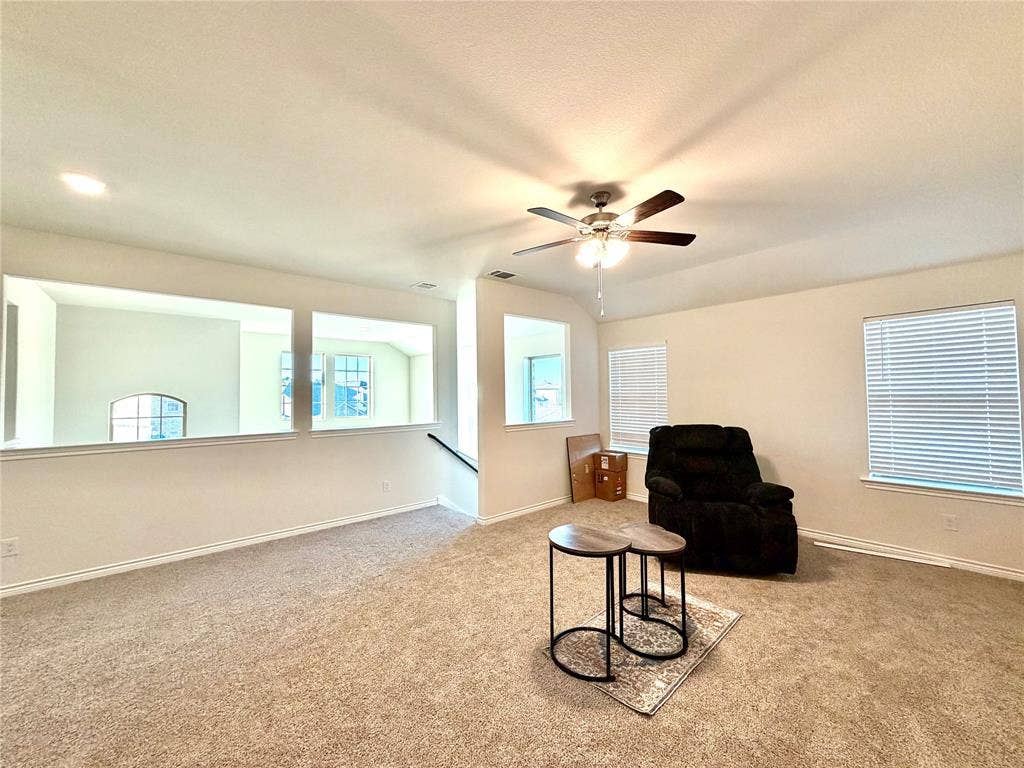 Open concept loft area featuring neutral carpeting, white walls, and a ceiling fan with integrated lighting