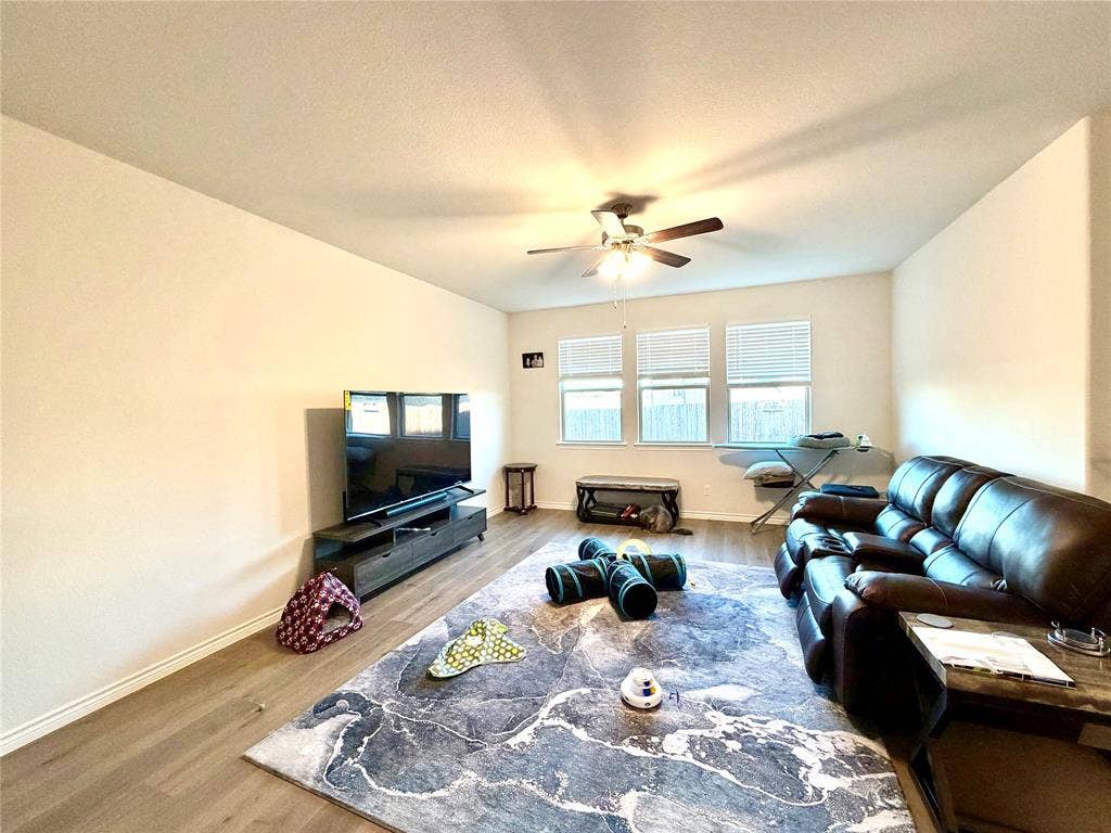 Spacious room with wood-finish flooring, ceiling fan, and multiple windows