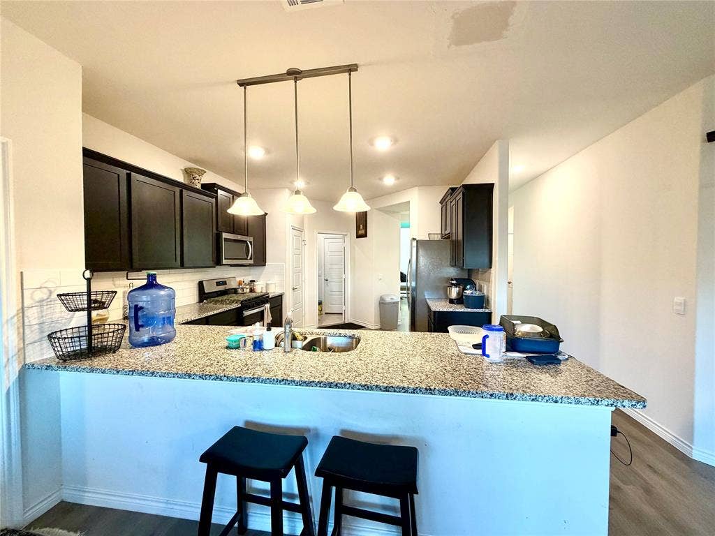 Kitchen featuring dark wood-finish cabinetry, granite-style countertops, stainless steel appliances, and recessed lighting