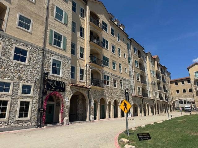 Multi-story building featuring stone and stucco exterior, arched walkways, decorative iron balconies, and prominent window shutters