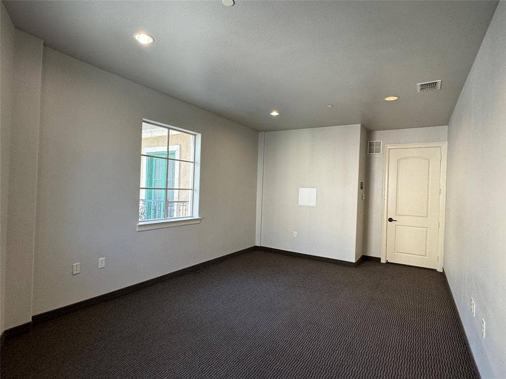 Recessed lighting, window with grid panes, neutral wall paint, dark patterned carpet, and paneled interior door