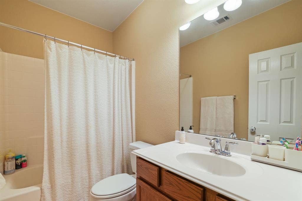 1213 Egret Court, Little Elm, TX 75068 Bathroom with a white tub and shower surround, a white toilet, and a vanity with a white countertop and wood-finish cabinetry