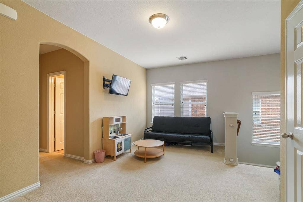 1213 Egret Court, Little Elm, TX 75068 Carpeted room with multiple windows, an arched entryway, and neutral-toned walls