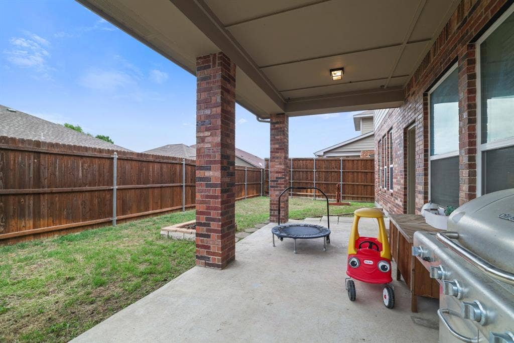 1213 Egret Court, Little Elm, TX 75068 Covered concrete patio with brick support columns, a wood privacy fence, and a built-in fire pit