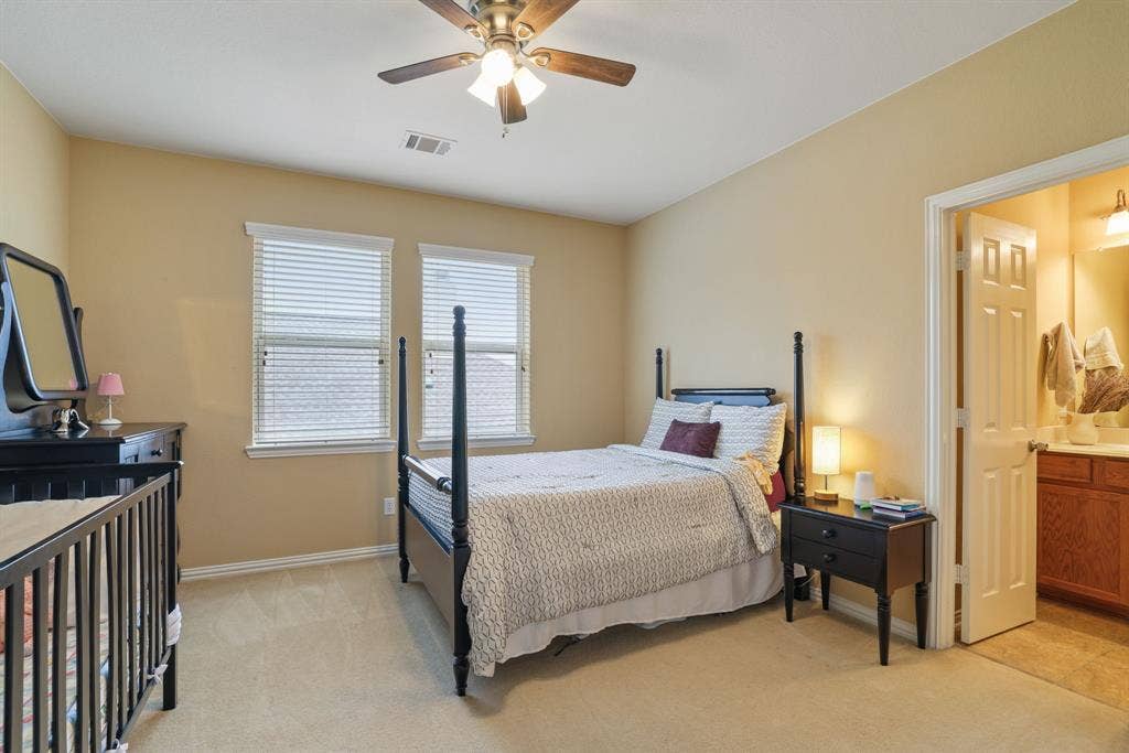 1213 Egret Court, Little Elm, TX 75068 Carpeted room with a ceiling fan, two windows with blinds, and an attached bathroom featuring a vanity with wood-finish cabinetry and a tiled floor