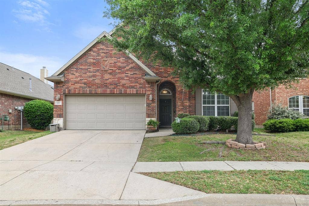 1213 Egret Court, Little Elm, TX 75068 Brick exterior with gabled roofline, arched entry, mature front tree, and attached garage