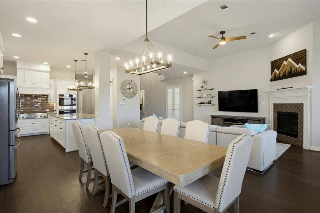 2721 Old Shire Path Road, Prosper, TX 75078 Open-concept living space featuring wood-finish flooring, a kitchen with white cabinetry and an island, a fireplace with a herringbone tile surround, and recessed lighting