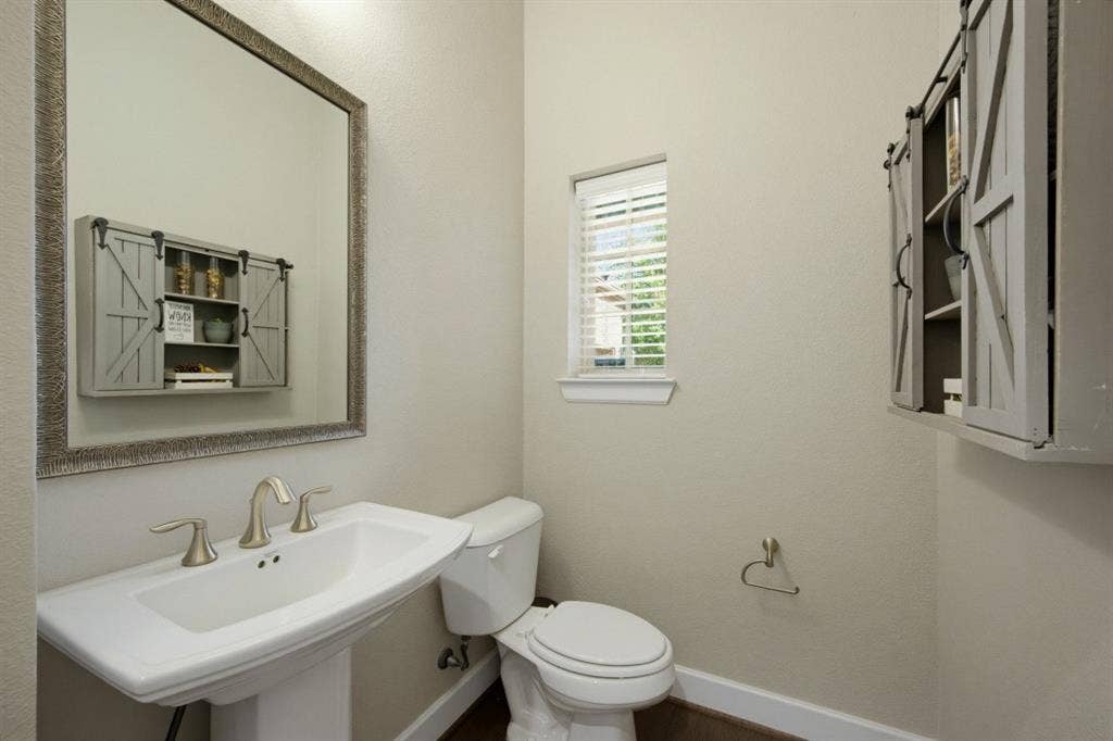 2721 Old Shire Path Road, Prosper, TX 75078 Pedestal sink with brushed nickel faucet, framed wall mirror, white toilet, and window with blinds