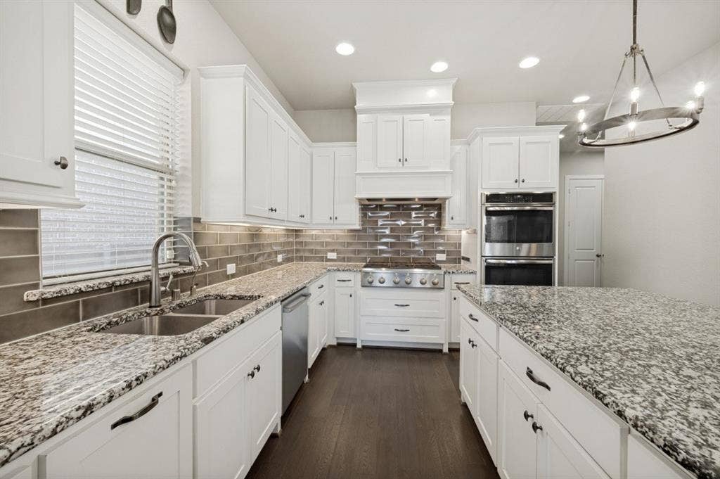 2721 Old Shire Path Road, Prosper, TX 75078 White cabinetry, granite countertops, stainless steel appliances, wood-finish flooring, and a decorative chandelier