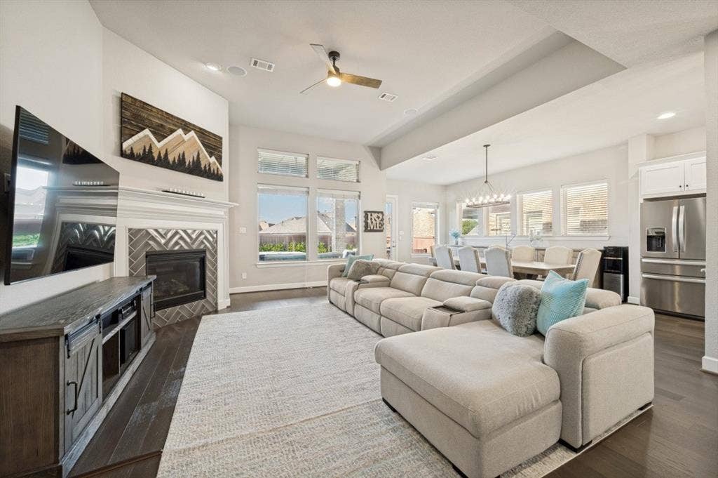 2721 Old Shire Path Road, Prosper, TX 75078 Living area featuring dark wood-finish flooring, a fireplace with a chevron-patterned tile surround and white mantel, and large windows with transom panels