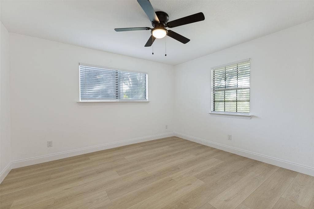 4721 Fallon Place, Dallas, TX 75227 Light-filled upstairs bedroom featuring two windows with blinds, luxury vinyl plank flooring, a ceiling fan with integrated lighting, and crisp white walls