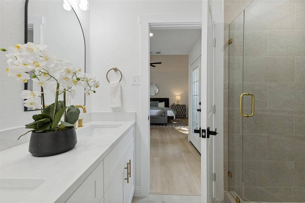 4721 Fallon Place, Dallas, TX 75227 Primary bath with a double vanity, gold-tone hardware, an expansive mirror, and a glass-enclosed shower