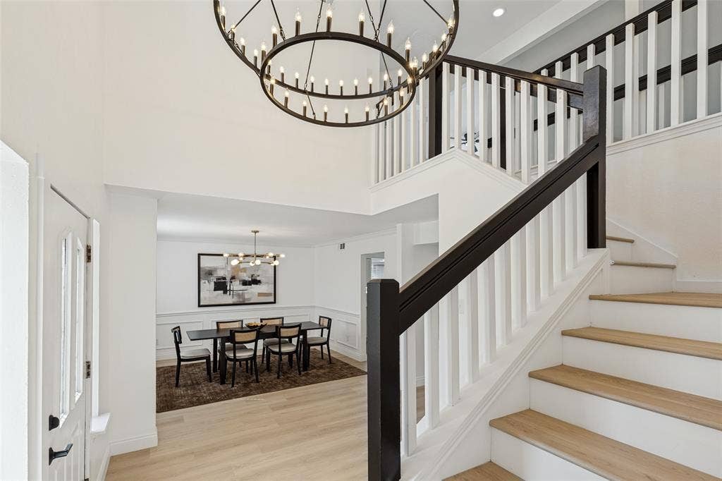 4721 Fallon Place, Dallas, TX 75227 Double-height foyer with a circular wrought iron chandelier, luxury vinyl plank flooring, and a two-tone staircase featuring white risers and dark wood handrails