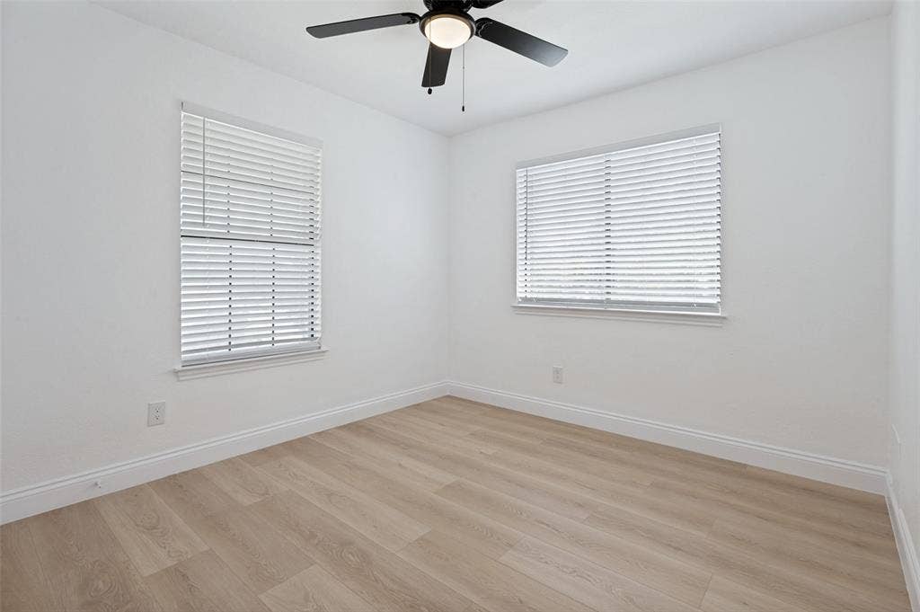 4721 Fallon Place, Dallas, TX 75227 Upstairs bedroom with luxury vinyl plank flooring, white walls, two windows with blinds, and a ceiling fan with integrated lighting
