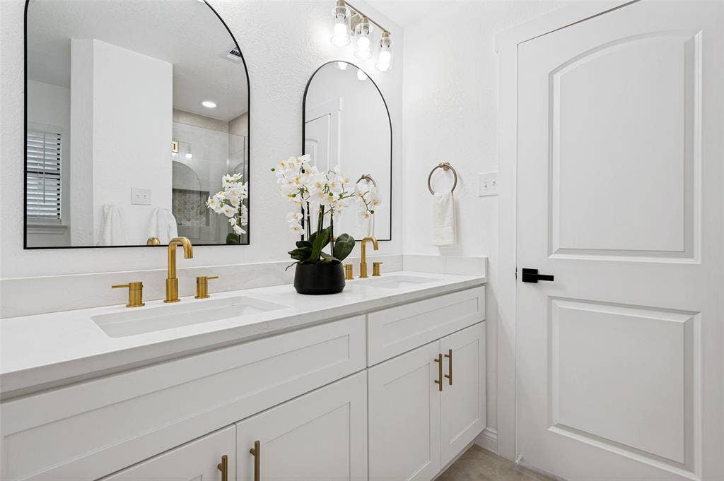 4721 Fallon Place, Dallas, TX 75227 Primary bath with dual arched mirrors, a white shaker-style double vanity, and gold-finish hardware