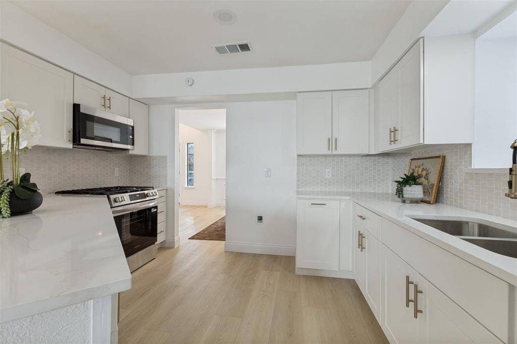 4721 Fallon Place, Dallas, TX 75227 White cabinetry with gold-tone hardware, luxury vinyl plank flooring, stainless steel appliances, quartz countertops, and a mosaic tile backsplash