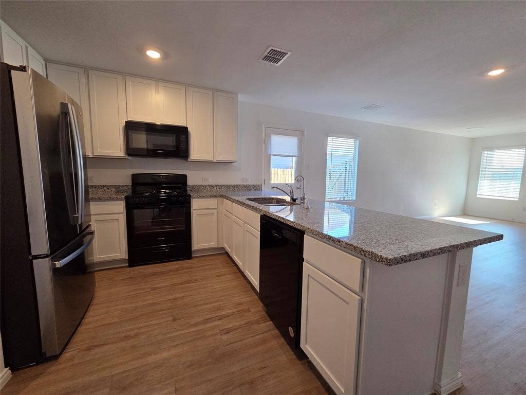 Kitchen featuring white cabinetry, granite countertops, black appliances, a stainless steel refrigerator, and wood-finish flooring