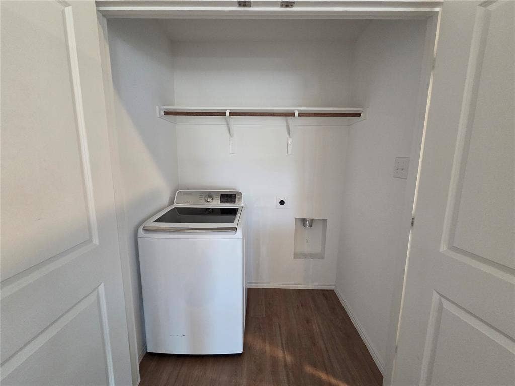 Dedicated laundry closet featuring a wood-finish flooring, built-in shelving, and a wall-mounted outlet