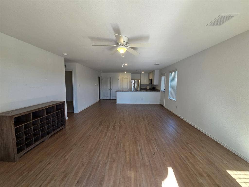 Open-concept living space with wood-finish flooring, white walls, and a ceiling fan